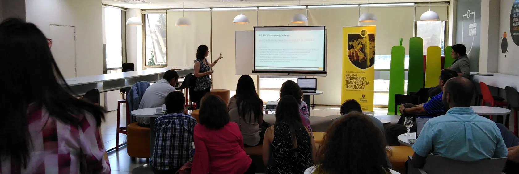 Una mujer exponiendo información ante un grupo de personas que le prestan atención.