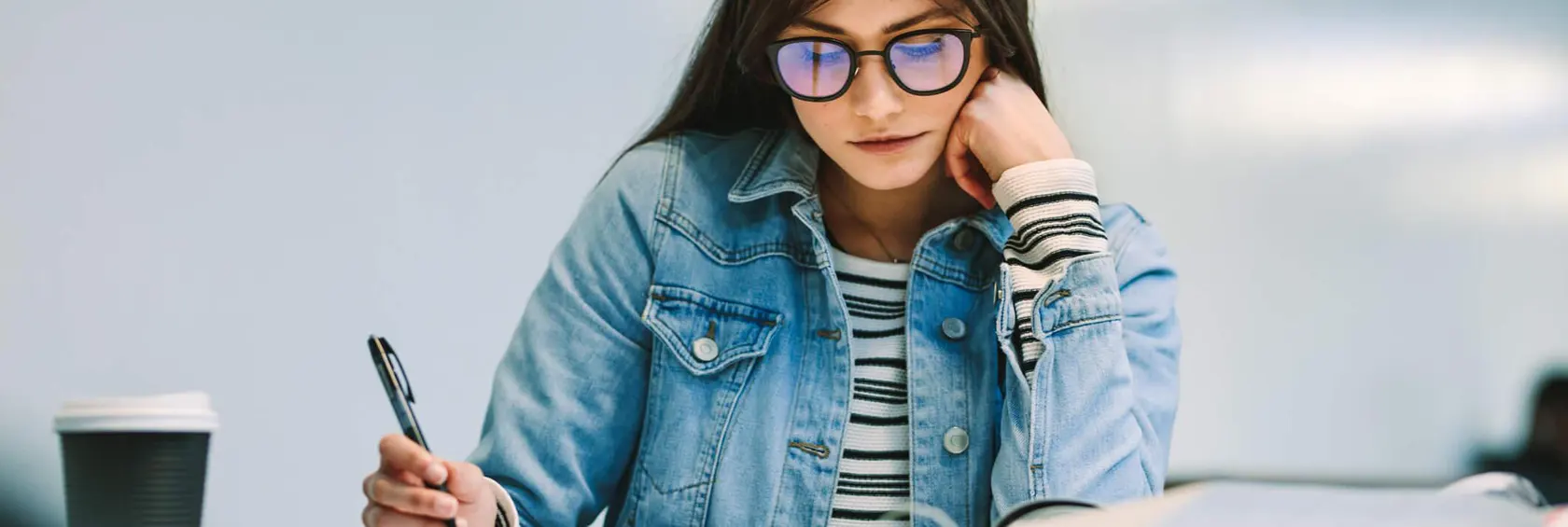 Mujer jóven escribiendo y apoyando su cabeza en su mano