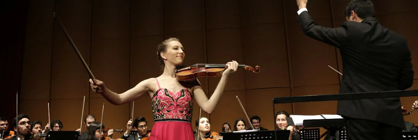 Violinista interpretando en un concierto sinfónico junto a una orquesta y su director.